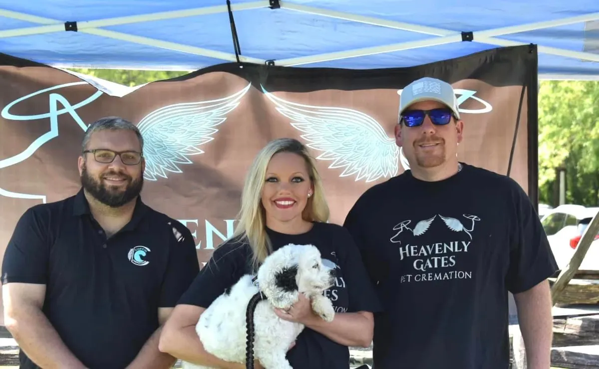 Kyle Coffin, Amy Ford and Jacob Ford smiling under a Heavenly Gates tent, with Amy holding a small white dog.